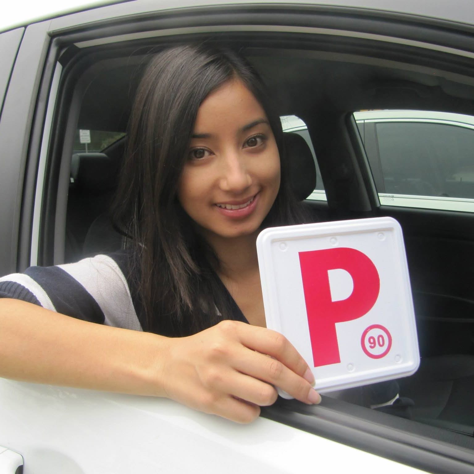 A successful driving school student standing outside the Service NSW registry hub building holding his official practical test pass sheet next to a red D-Tech instructor vehicle.