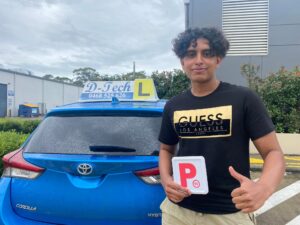 A smiling local student holding up her new NSW provisional Red P-Plate from the driver's side window of a white vehicle after passing her driving test.