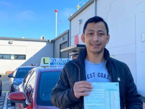 A successful adult migrant student standing outside a Service NSW registry hub entrance next to a branded D-Tech instructor vehicle, illustrating an overseas license conversion with no provisional plates.