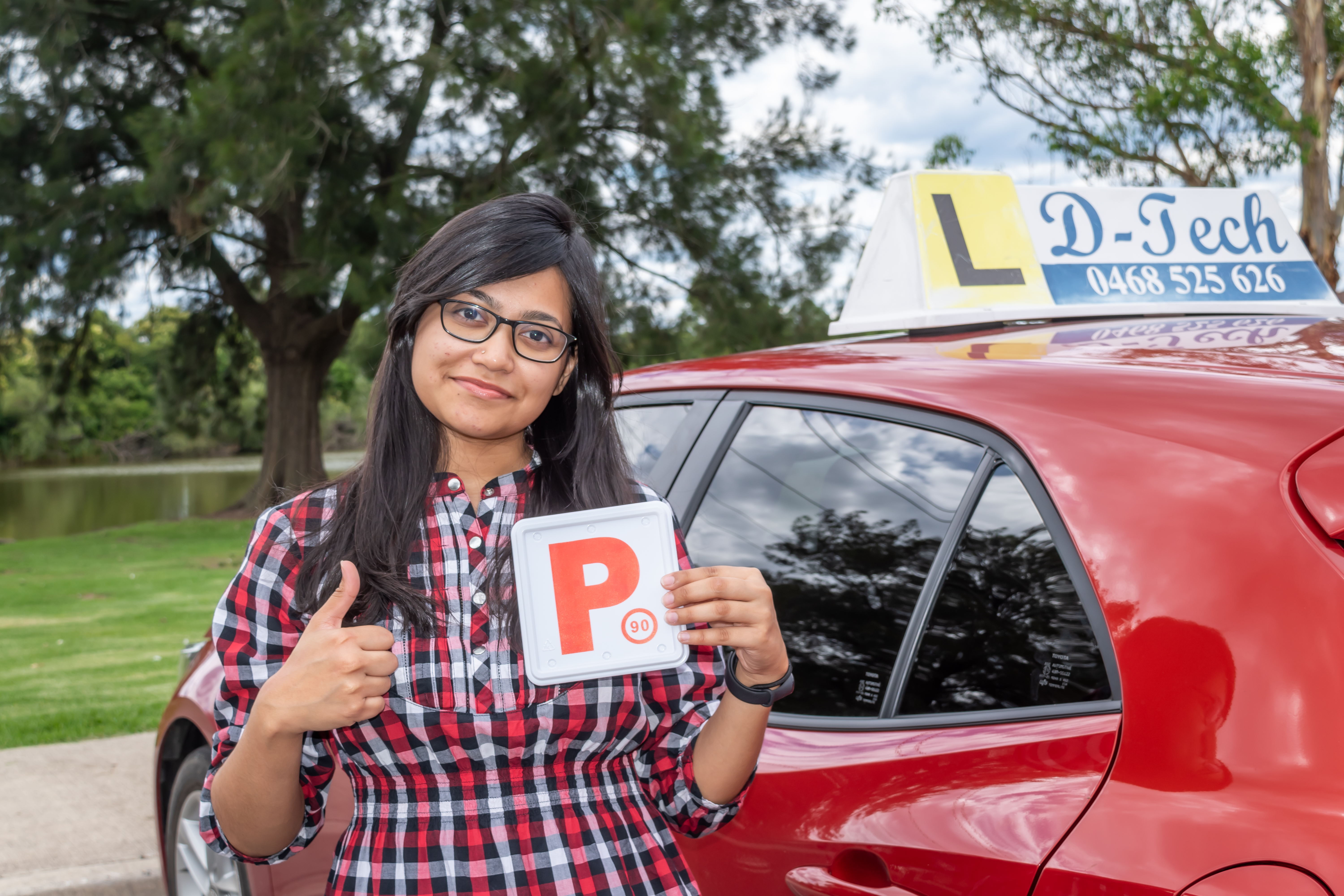 Smiling driving student showing off her fresh P-plate next to a red driving training car window