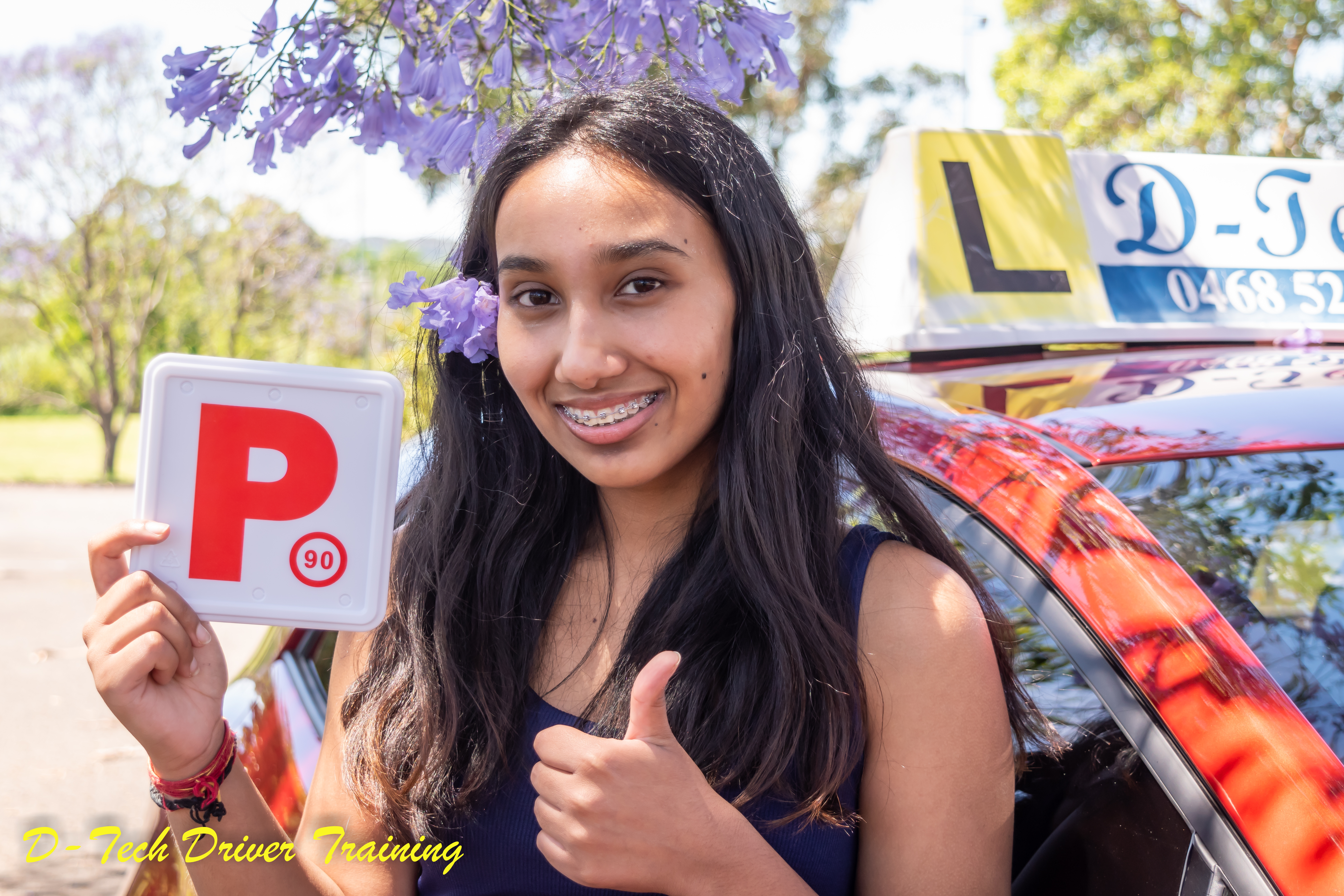 Smiling teenage student showing her fresh P-plate with purple blossoms behind her ear