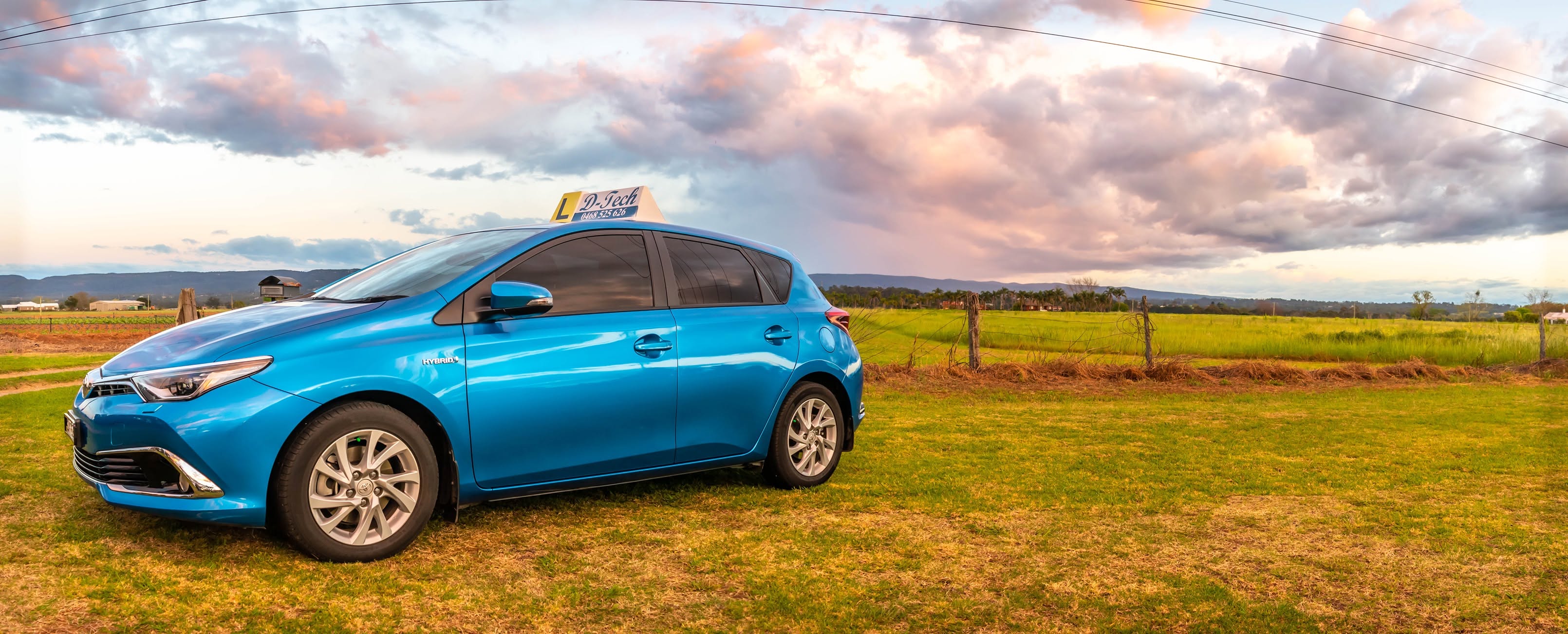 D-Tech training car driving down the wide open rural fields of Drift Road in Richmond under a colorful sunset sky