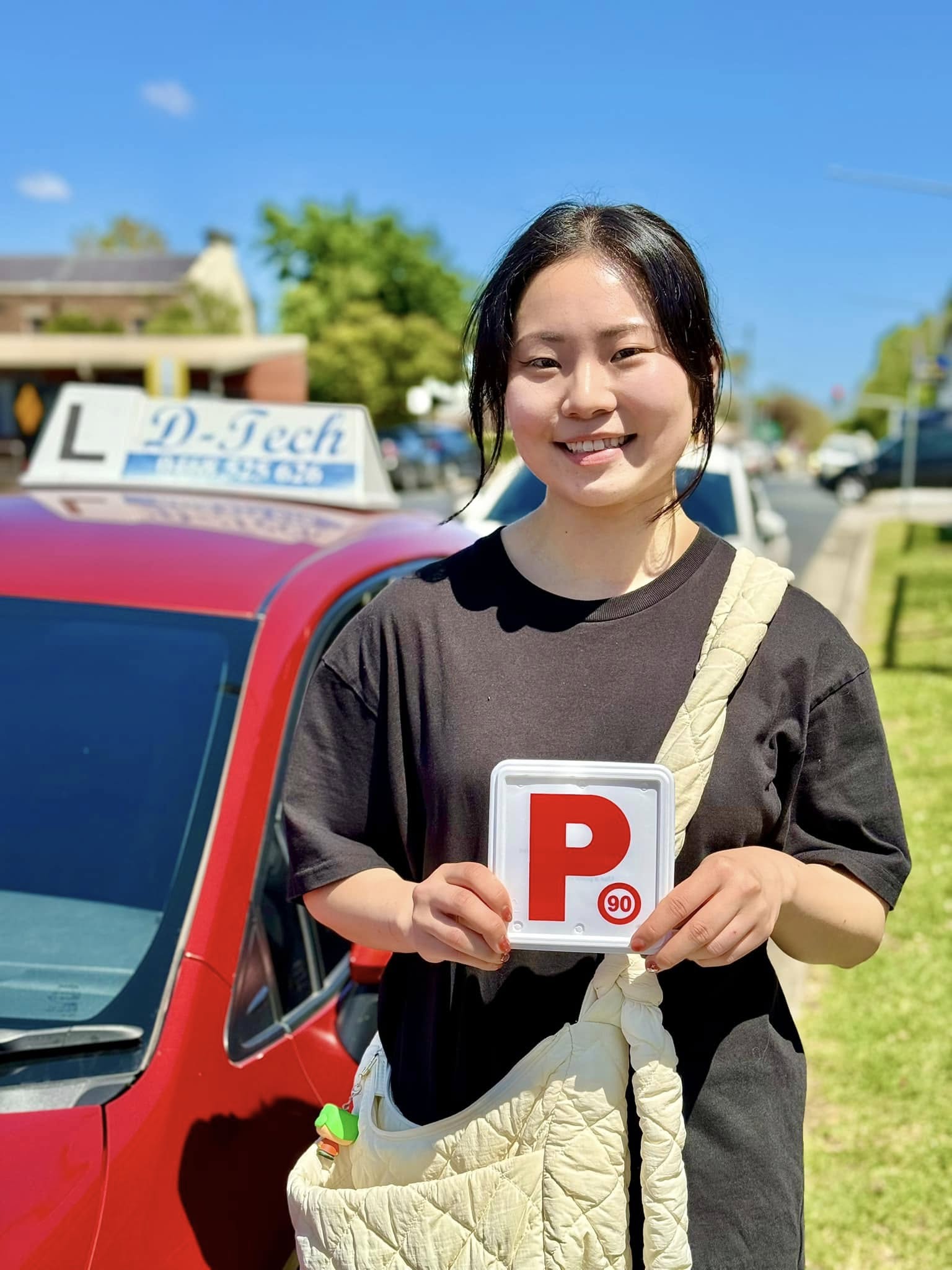 D-Tech Driver Training student smiling and holding her new NSW P-plates next to the D-Tech driving school car after passing her practical test in Grantham Farm.