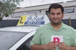 Smiling woman proudly holding a red P-plate above her head next to a white D-Tech driver training car sign.