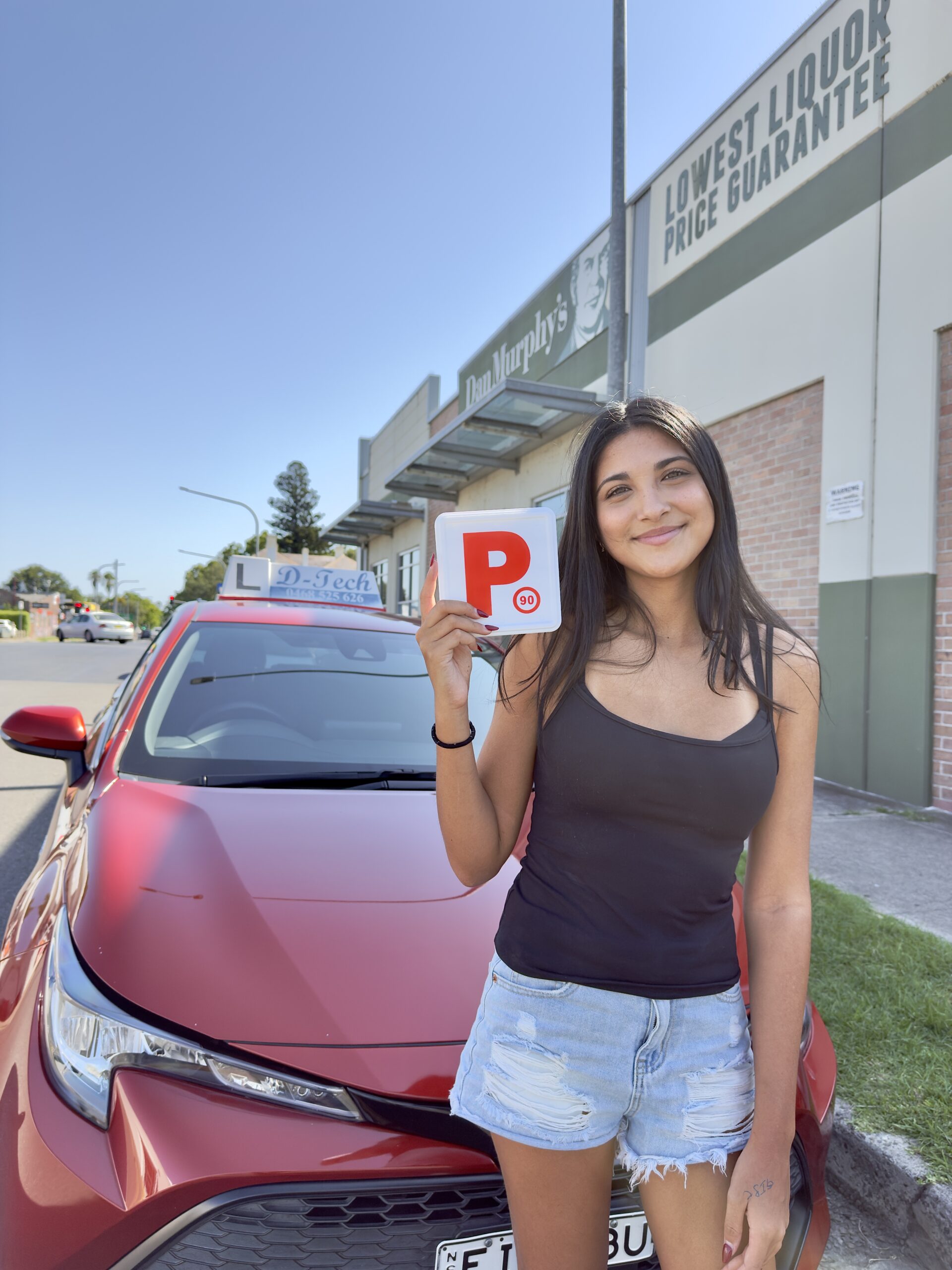 D-Tech Driver Training student Amilia smiling and holding her P-plate outside the testing centre with a Hawkesbury driving school.