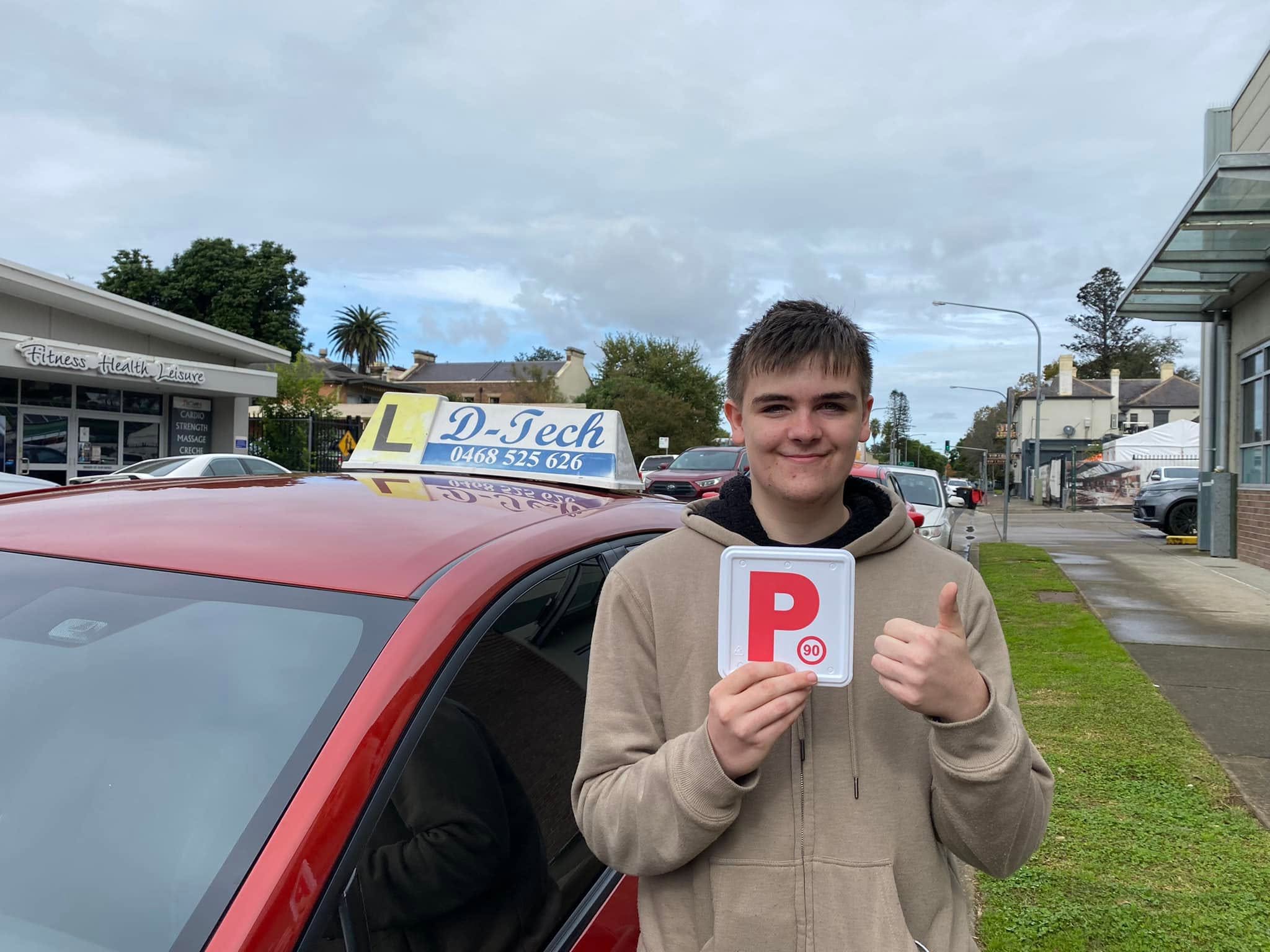 D-Tech Driver Training student Peter holding his P-plate after passing his practical driving test at Richmond Service NSW.