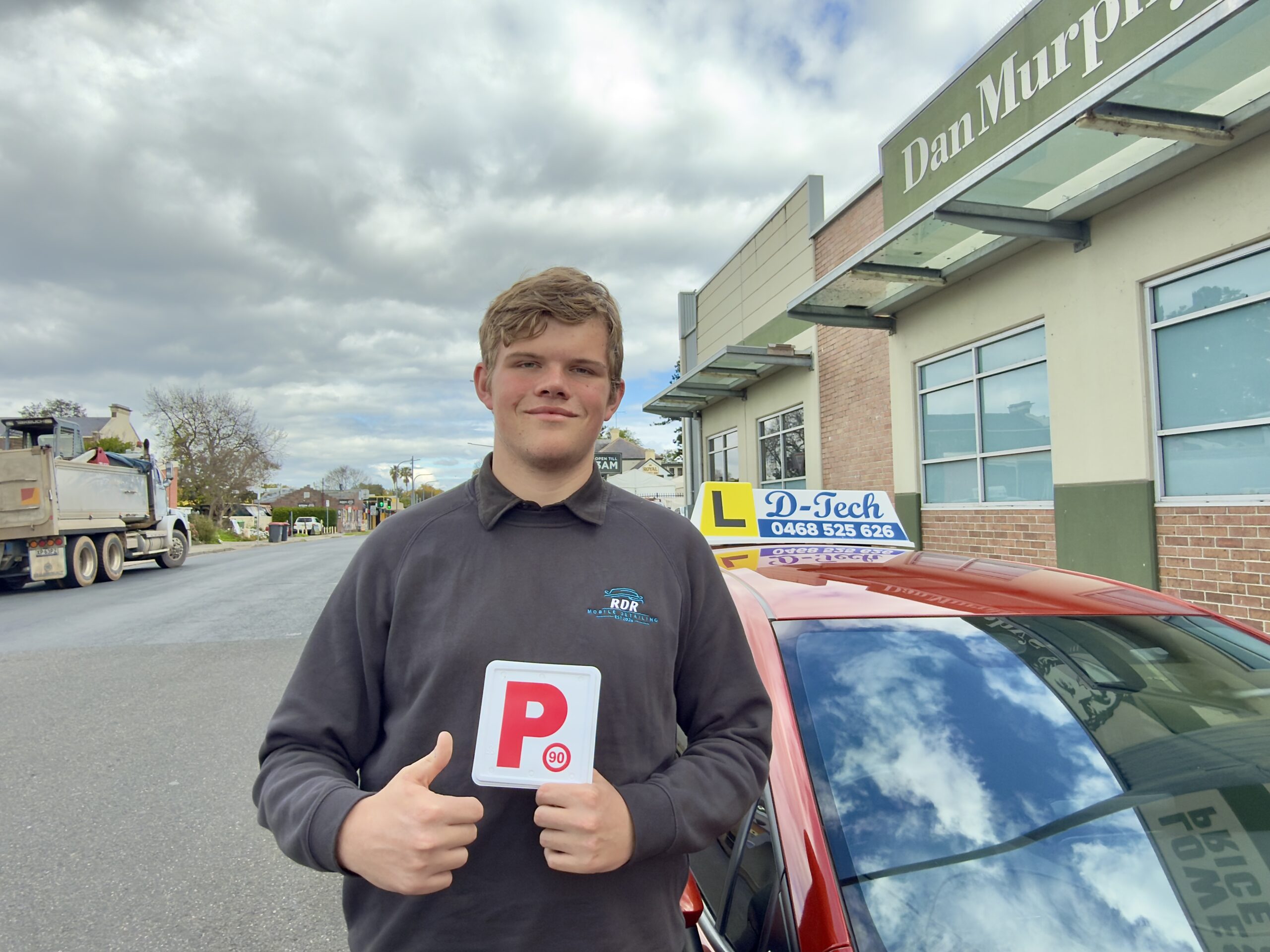 Ryan proudly holding P-plate in front of D-Tech dual-control training car in South Windsor.