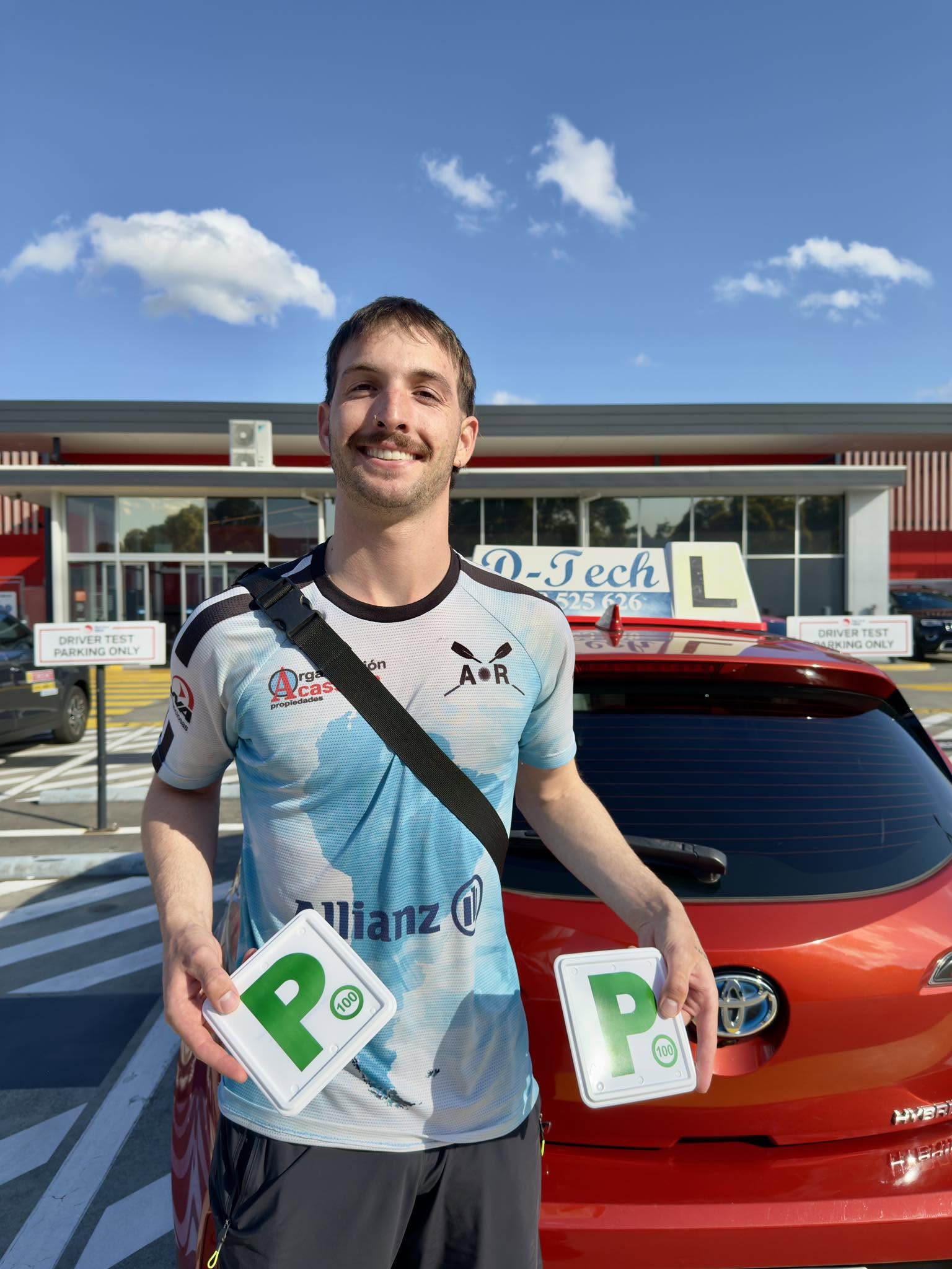 Successful learner driver holding green P-plates after passing the driving test at Castle Hill Service NSW HomeCo rooftop car park.