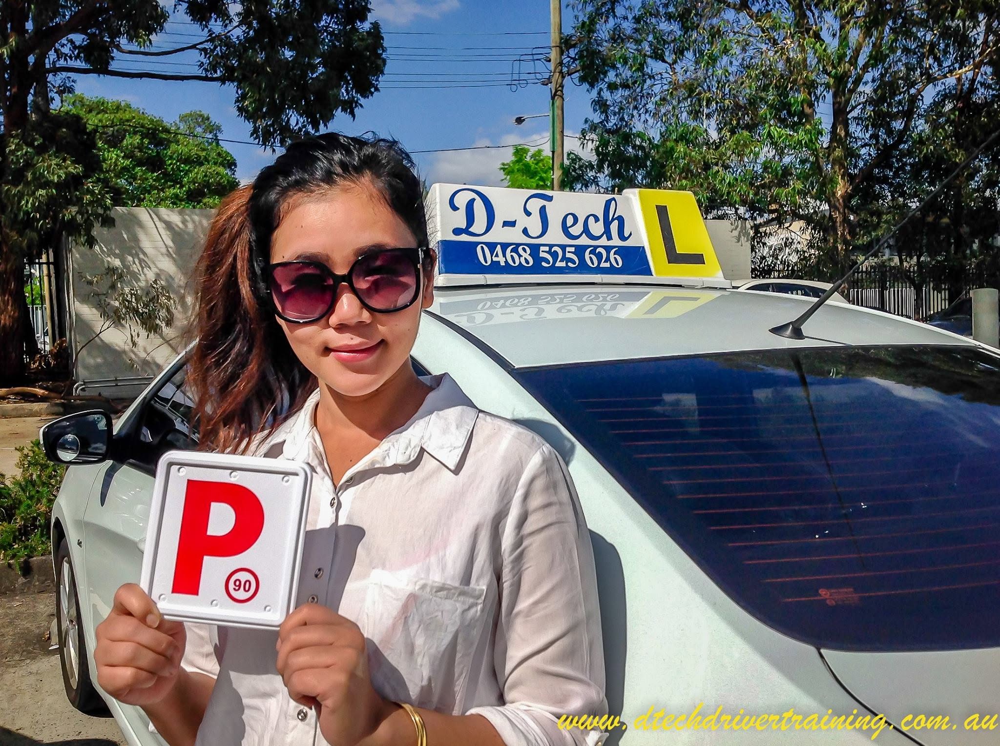Student Seng Htui smiling and wearing sunglasses while holding her red P-plate after passing her practical driving test in Blacktown.