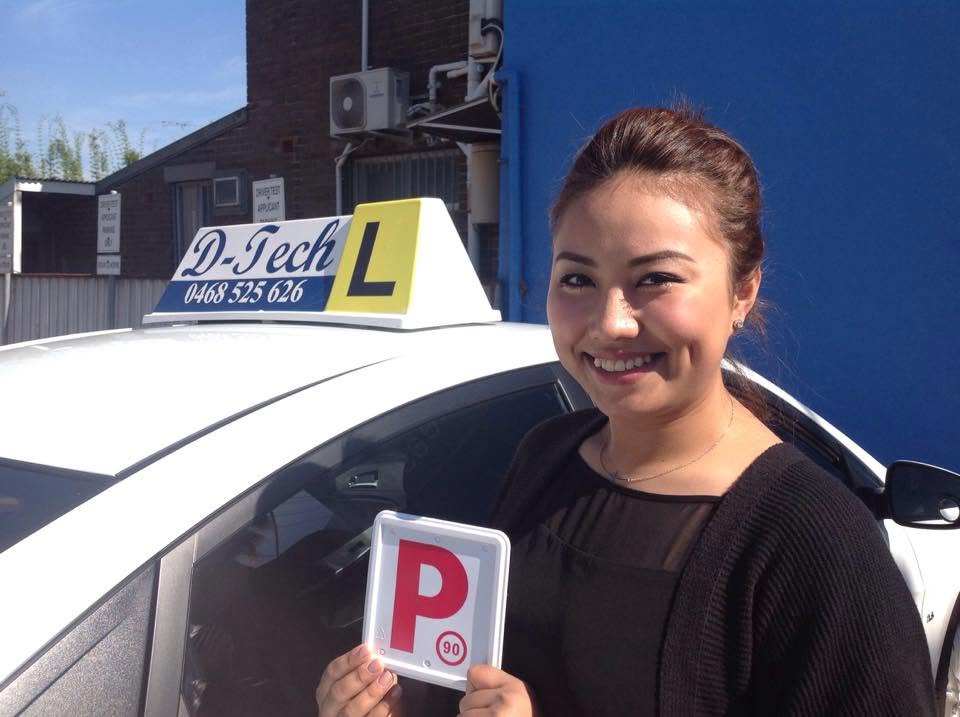 Student Shwe Hmone smiling happily as she holds her red P-plate beside the D-Tech dual-control training car.