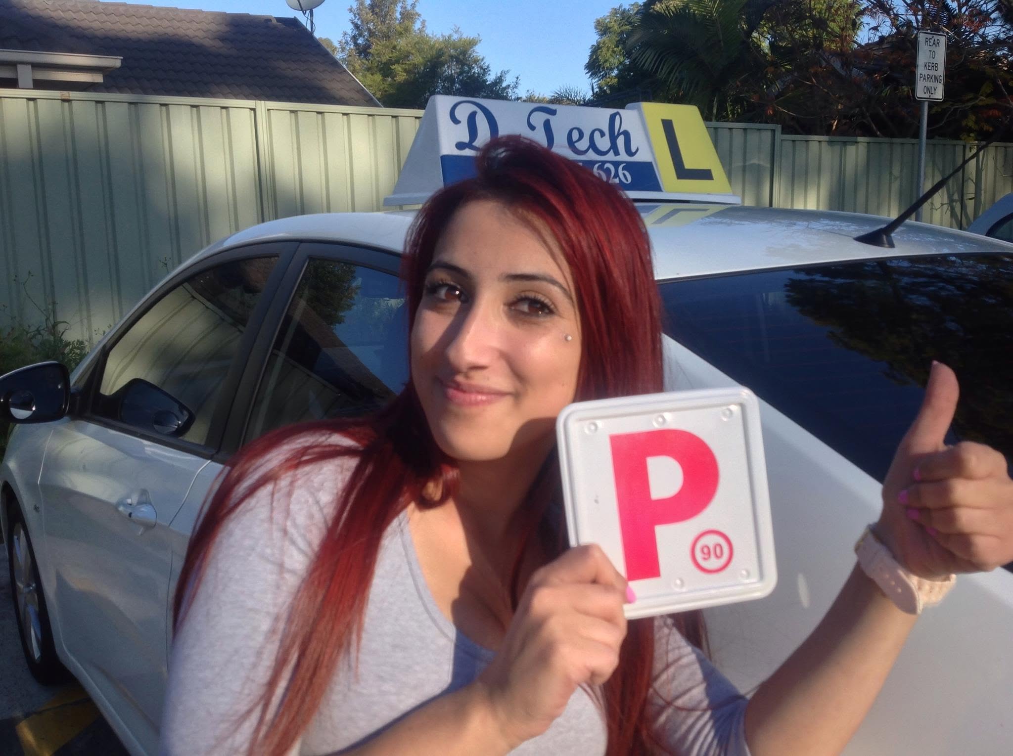 Happy student giving a thumbs up and holding her red P-plate after passing her practical driving test in Blacktown.